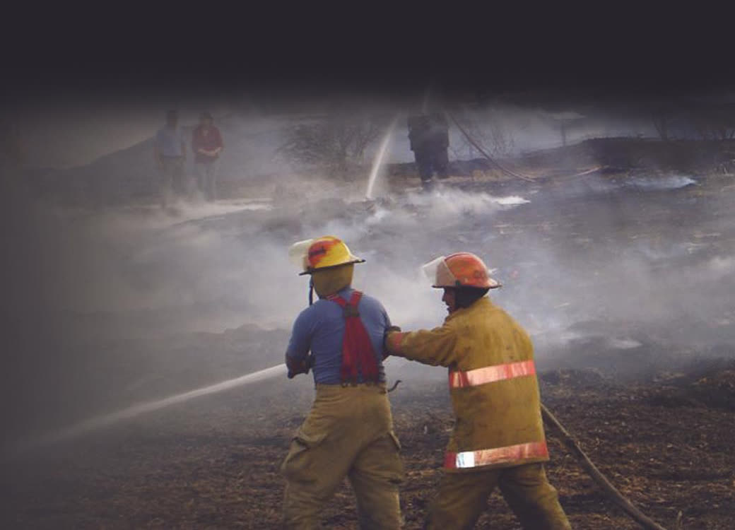 Dos bomberos sofocando un incendio de pastizal con una manguera